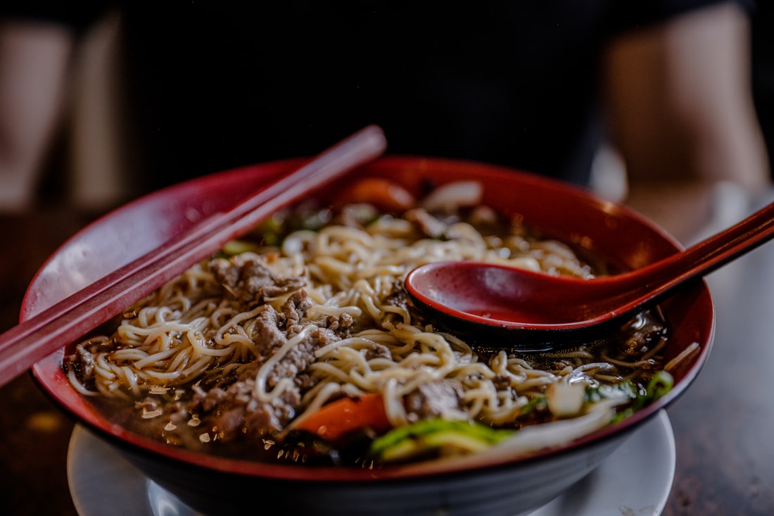 A richly colored Vietnamese noodle soup with herbs and chili oil glistening on the surface